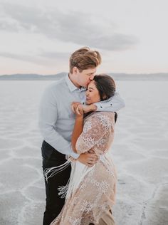 a man and woman standing next to each other on the beach in front of water