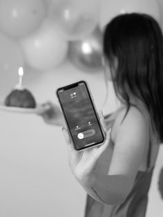 a woman holding up a cell phone in front of balloons