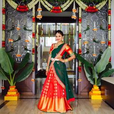 a woman standing in front of a doorway wearing a green and orange lehenga