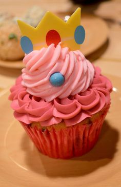 a cupcake with pink frosting and a crown on top sits on a plate