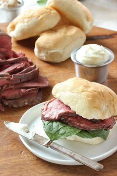 a corned beef sandwich on a plate next to bread rolls