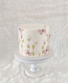 a white cake with pink flowers on it sitting on a table next to a white furnishing