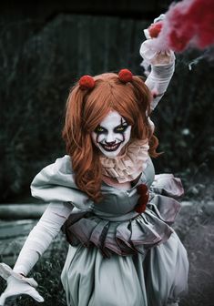 a woman dressed as a scary clown with red hair and white makeup, holding her arms out in the air