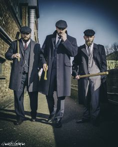 three men standing next to each other in suits and ties, one holding a cane