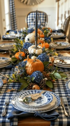 the table is set with blue and white plates, silverware, and pumpkins