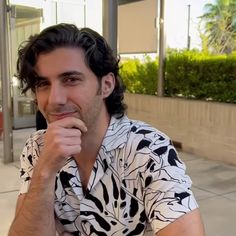 a man sitting on the ground with his hand under his chin and looking at the camera