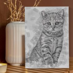 a black and white photo of a kitten sitting on a table next to a vase