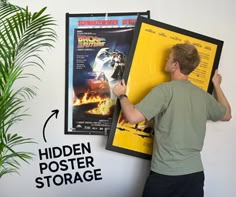 a man holding up a movie poster in front of a white wall with the words hidden poster storage below it