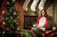 a woman sitting in front of a christmas tree with stockings hanging over her fireplace and presents on the mantel