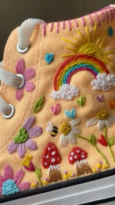 a pair of shoes with embroidered flowers and rainbows on the side, sitting on a shelf