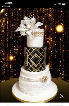 a three tiered cake with black and white decorations on top, surrounded by golden lights