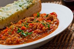 a white plate topped with meat and beans covered in sauce next to a slice of bread