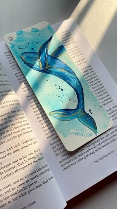 an open book with a blue mermaid tail on the cover and watercolor paint splatters all over it