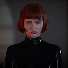 a woman with red hair wearing a black latex outfit in a dimly lit room