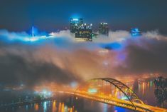 the city lights shine brightly in the foggy night sky over a river and bridge