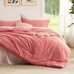 a bed with pink sheets and pillows in a room next to two pictures on the wall