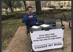 a man sitting at a table with a sign on it that says change my mind