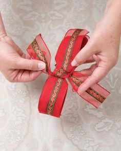 two hands holding red ribbon with green and gold trim