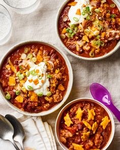 three bowls of chili with sour cream on top and two spoons next to them