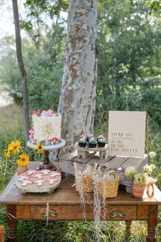 a table topped with cakes and cupcakes next to a forest filled with trees