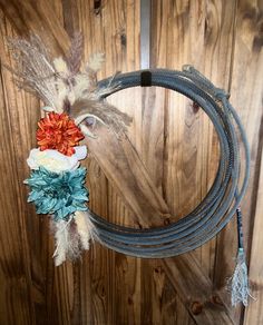 a rope with flowers and feathers on it hanging from the side of a wooden wall