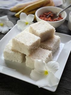 three pieces of rice cake on a white plate with flowers and spices in the background