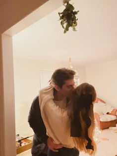 a man and woman standing in a living room next to each other with christmas lights on the ceiling