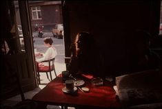 two people sitting at a table in front of an open door looking out onto the street