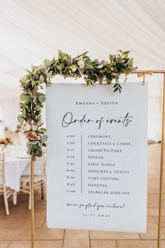 a white sign with greenery on it sitting in front of a table and chairs