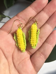 a hand holding a pair of earrings with yellow and green corn on the cob