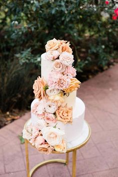 a three tiered wedding cake with flowers on the top and bottom is sitting on a gold stand