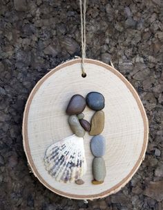 a wooden ornament with rocks and shells on it hanging from a rope against a rock wall