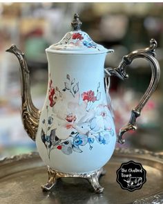 an ornately decorated tea pot sitting on top of a silver tray with flowers painted on it