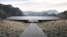 an empty walkway leading to a wooden structure in the middle of a field with mountains in the background