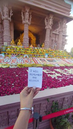 a person holding up a sign in front of a building with flowers all over it