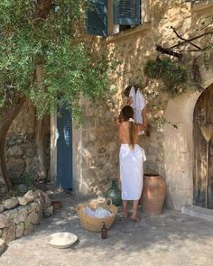 a woman standing in front of a stone building next to a potted planter