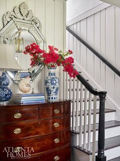 red flowers are in vases on a dresser next to a mirror and staircase railing