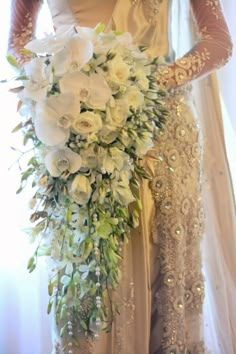 a woman in a wedding dress holding a bridal bouquet with white flowers and greenery