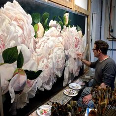 a man is painting flowers on a large piece of art