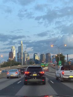 cars are driving down the highway in front of tall buildings and skyscrapers at dusk