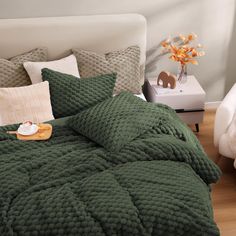 a bed with green comforter and pillows on it in a room next to a white chair