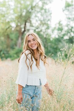 a woman standing in tall grass smiling at the camera