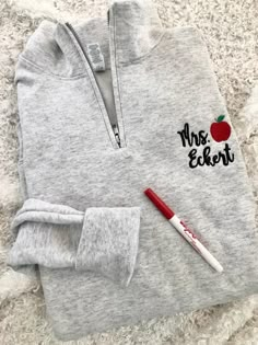 an apple embroidered on the back of a gray sweatshirt with a red pen next to it