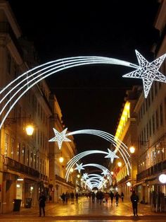 people are walking down an empty street with christmas lights on the buildings in the background