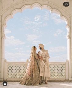 two people standing next to each other in front of a white arch and blue sky