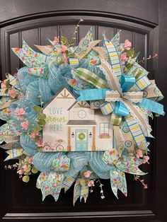 a wreath that has been decorated with flowers and ribbons on the front door to say love is here