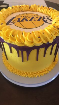 a lakers cake with yellow icing and purple swirls on the top is sitting on a table