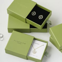 three green boxes with jewelry in them sitting on a table next to a pair of scissors