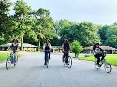 three people riding bikes down the street in front of some houses with trees on either side