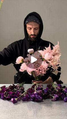 a man in a hoodie arranging flowers on top of a table with purple petals